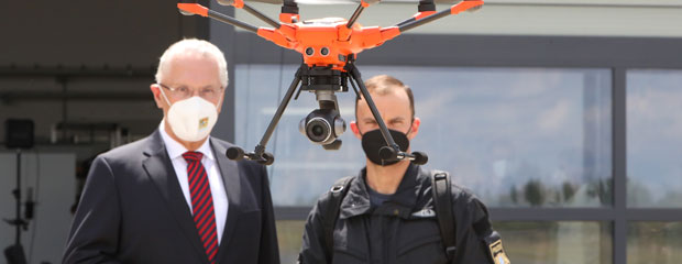 Innenminister Joachim Herrmann und ein Polizist betrachten eine fliegende Drohne