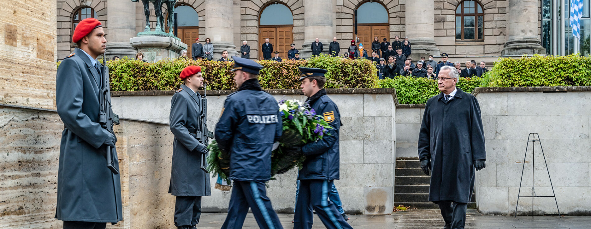 zwei Polizisten bei Kranzniederlegung, Innenminister Joachim Herrmann geht hinterher