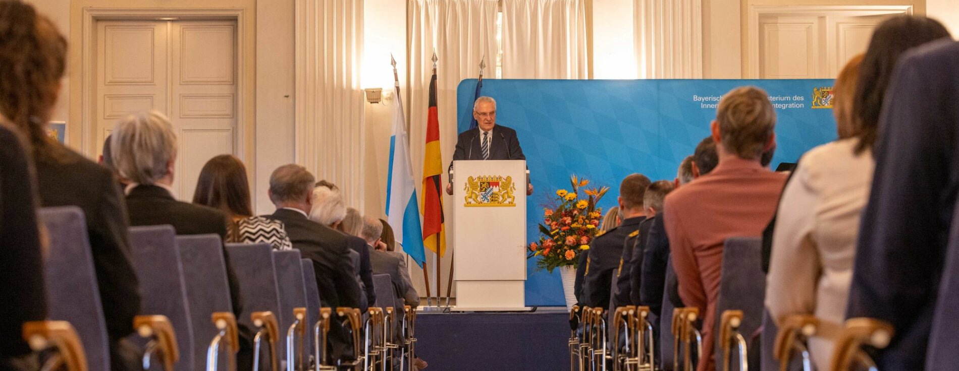 19. Dezember 2024: Innenminister Joachim Herrmann hat den scheidenden Präsidenten des Bayerischen Landesamtes für Verfassungsschutz, Herrn Dr. Burkhard Körner, aus dem Amt verabschiedet und dessen Nachfolger Manfred Hauser feierlich in sein neues Amt eingeführt. Herrmann: „Mit Dr. Burkhard Körner verlieren wir einen Verfassungsschützer mit Leib und Seele. Deshalb freue ich mich, dass wir mit Manfred Hauser einen idealen Nachfolger für ihn gefunden haben.“ Auf dem Bild ist Innenminister Joachim Herrmann bei seiner Rede anlässlich des Präsidentenwechsels beim LfV zu sehen, im Vordergrund sind man die Stuhlreihen mit den Ehrengästen.