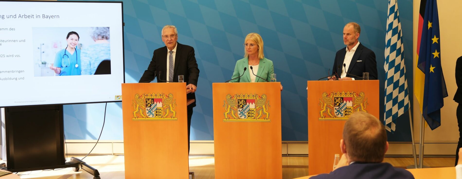 Auf dem Bild sind Innenminister Joachim Herrmann, Arbeitsministerin Ulrike Scharf sowie Dr. Markus Schmitz (Agentur für Arbeit) bei ihrer gemeinsamen Pressekonferenz zu sehen.