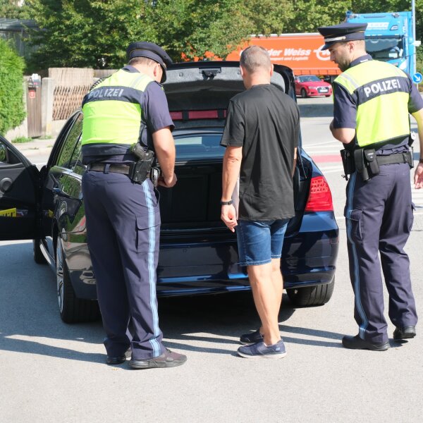 Zwei Polizisten lassen sich von einem Fahrer den Kofferraum zeigen