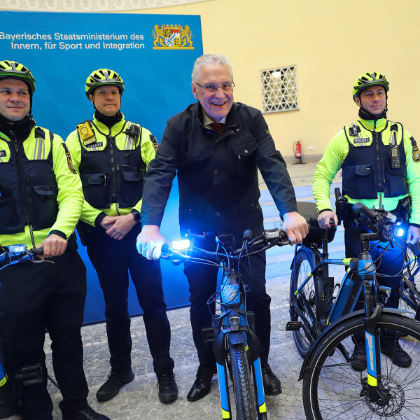 Herrmann auf Polizeirad mit Blaulicht zwischen Polizeiradlern vor Pressewand