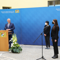 Innenminister Herrmann bei Pressekonferenz neben zwei Eingebürgerten