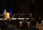 Blick vom Saal auf die Bühne, auf der Innenminister Joachim Herrmann hinter dem Rednerpult steht und das Saxophon-Quartett des Polizeiorchesters Bayern sitzt