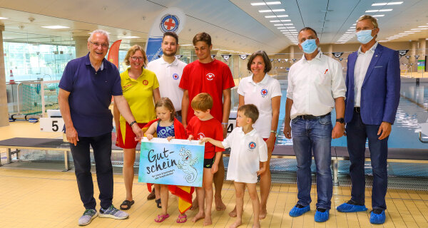 Sportminister Joachim Herrmann mit Vertretern der Wasserwacht, DLRG und des Bayerischen Schwimmverbandes und Kindern mit großem Gutschein